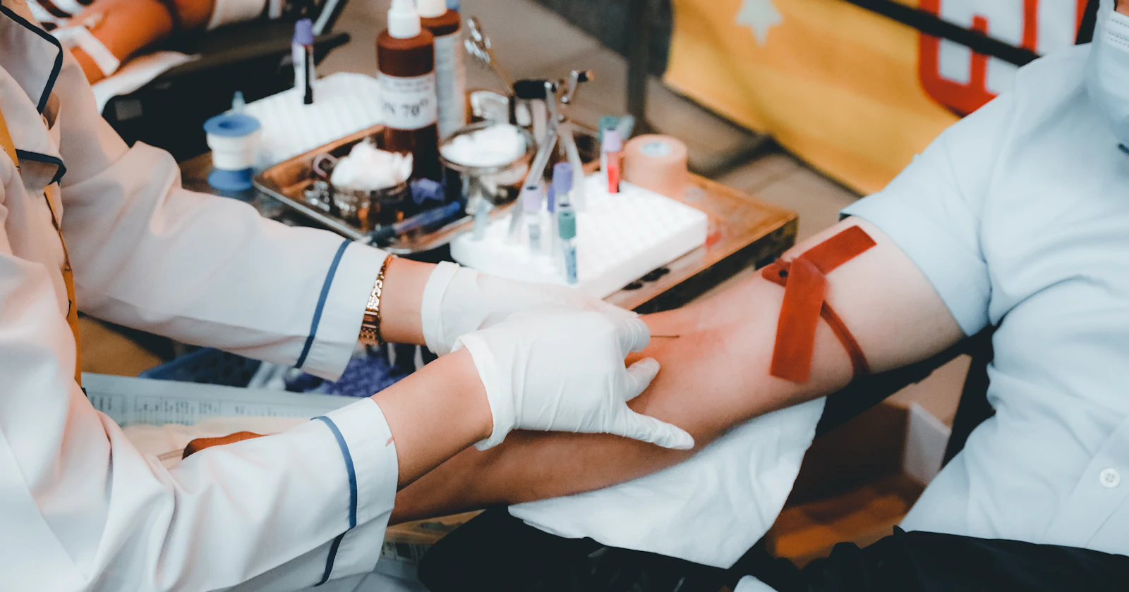 A phlebotomist in gloves drawing blood from a patient’s arm, with a tourniquet in place.